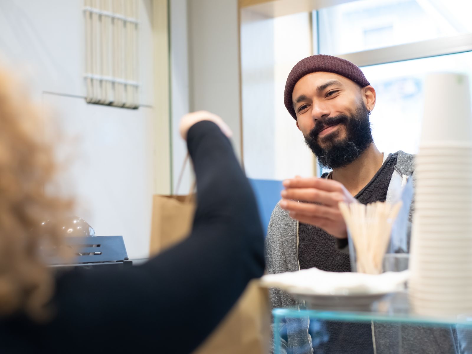 A shopkeeper handing a paper bag across the counter to a customer.