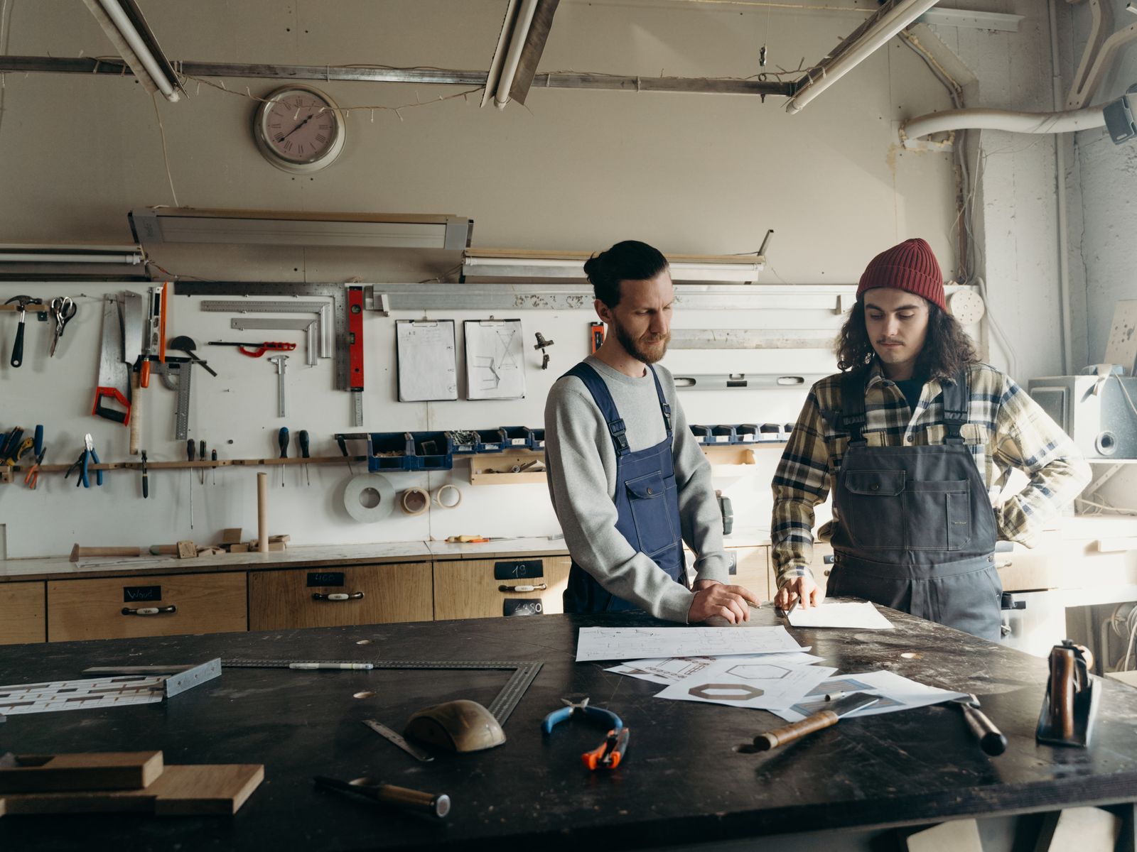 Two people leaning over drawings spread across a workbench, working something out together.